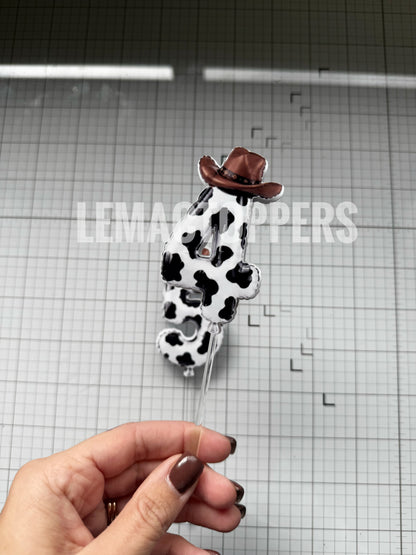 A Cow-Print Cake Topper That looks like a balloon number, with a brown cowboy hat